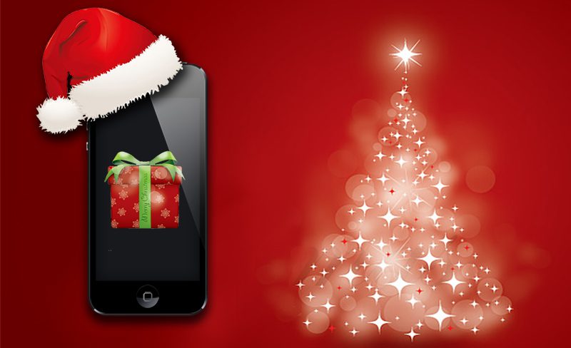 A smartphone wearing a Santa hat displays a wrapped gift on its screen, set against a red background with a glowing, stylized Christmas tree made of light spots.