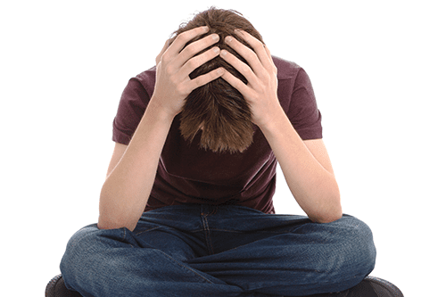 A person sitting cross-legged with their head down and hands covering their head, appearing distressed or upset, against a white background.