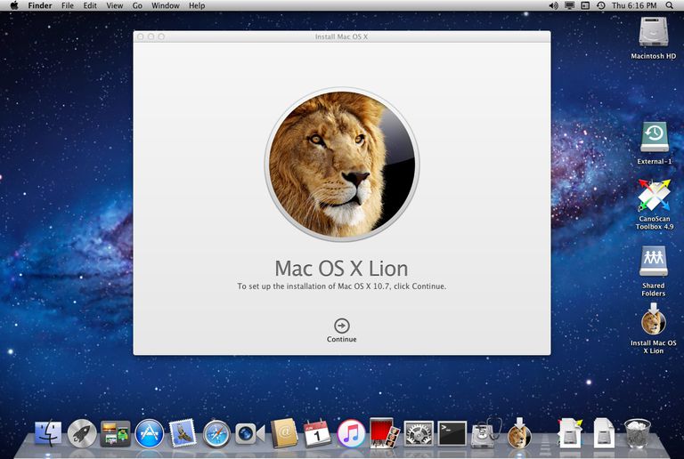 A Mac computer screen displaying the Mac OS X Lion installation window, featuring a lion’s face and a "Continue" button, with desktop icons and a starry night sky wallpaper in the background.