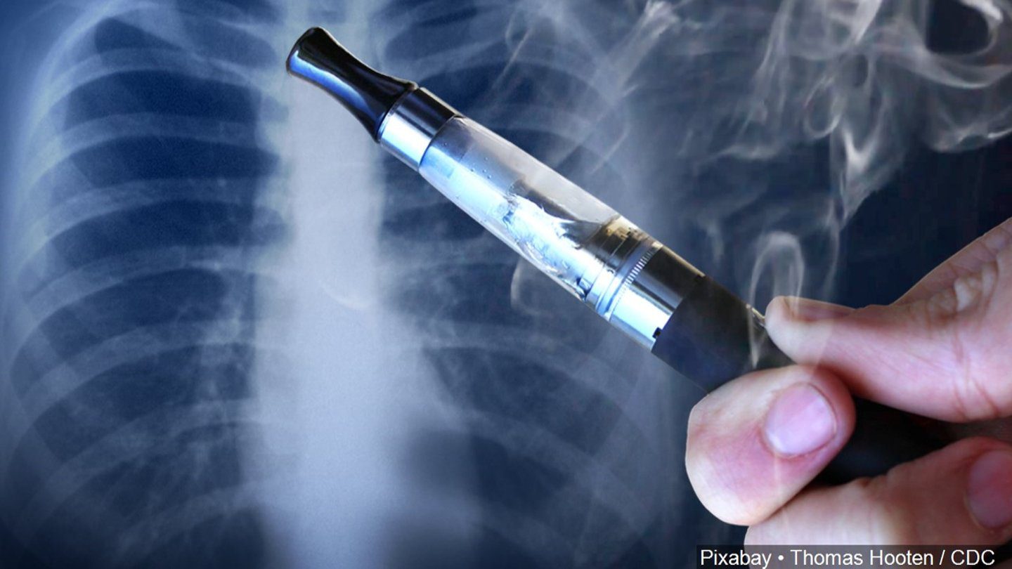 A hand holding a vape pen with smoke rising in front of a chest X-ray image, suggesting the impact of vaping on lung health.