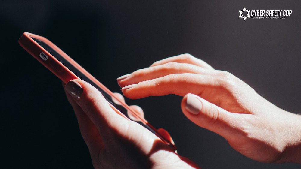 A close-up of a person’s hands using a smartphone, with the logo and text “Cyber Safety Cop” and “Your Safety Solution, LLC” in the upper right corner.