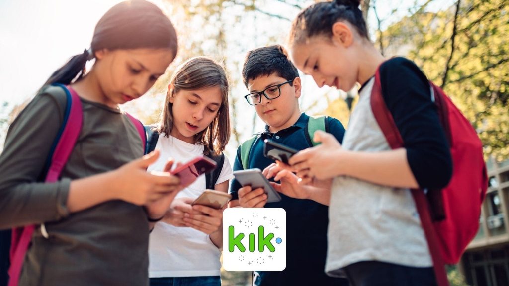 Four children with backpacks stand outdoors, closely looking at their smartphones as sunlight filters through the trees. The Kik Messenger logo is visible in the foreground, highlighting ongoing safety concerns about messaging apps for kids.