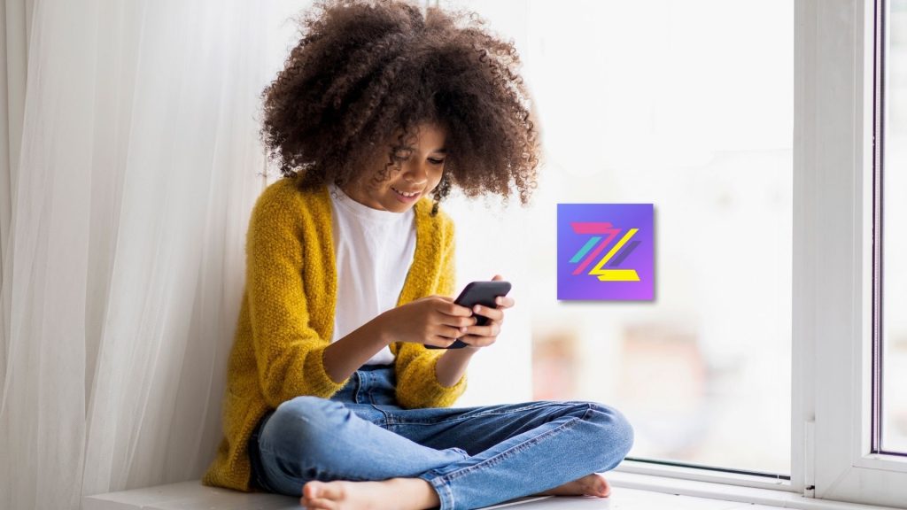 A child with curly hair, wearing a yellow cardigan and jeans, sits cross-legged on a windowsill, smiling while using the Zigazoo app on a smartphone. A colorful abstract logo appears on the window beside them.