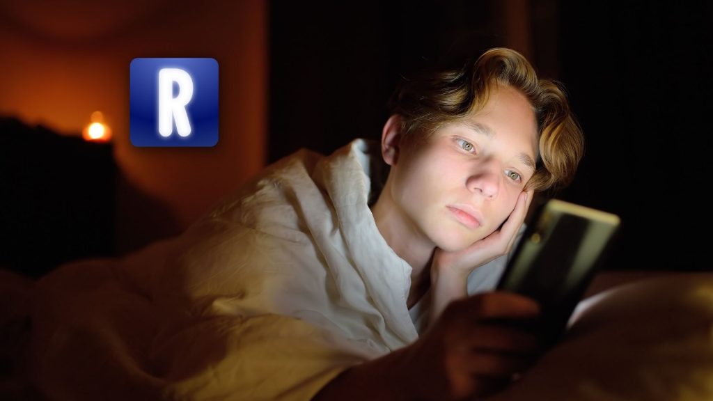 A young person wrapped in a white blanket lies in bed at night, looking thoughtfully at a smartphone. In the background, a glowing "R" icon hints at an AI Companion—perhaps suggesting a late-night Replika App review. The room is dimly lit.